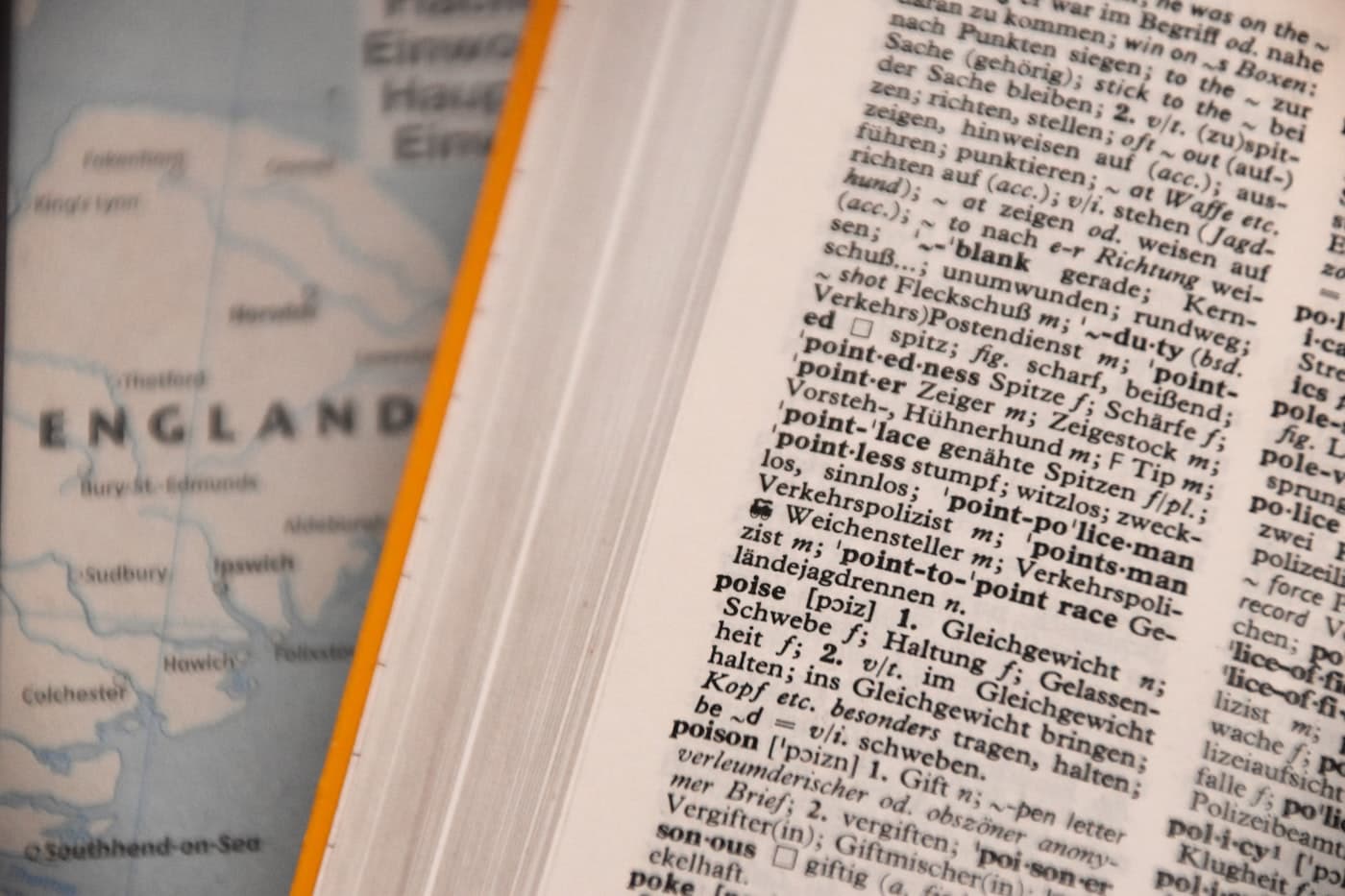 Diccionario de inglés y alemán abierto junto a un mapa de Inglaterra, material de idiomas de muestra
