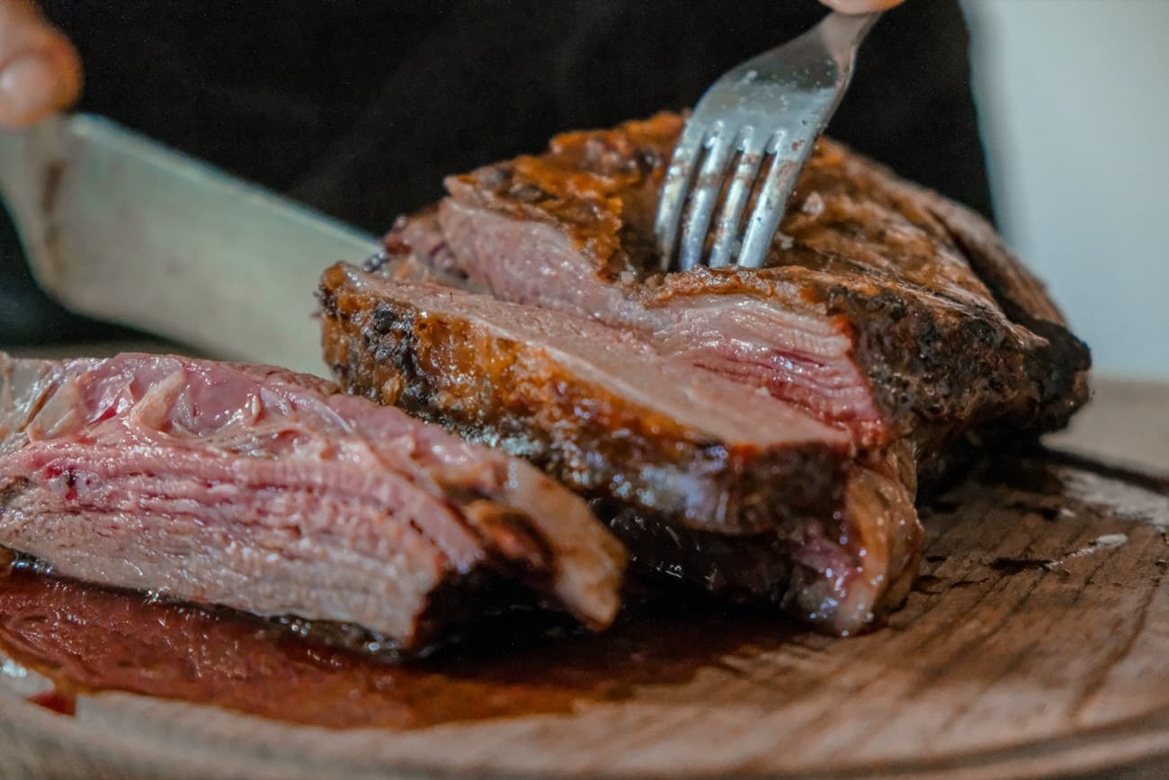 Chuleta madurada de vaca vieja recién cortada sobre tabla de madera, con su jugo. Plato de muestra.