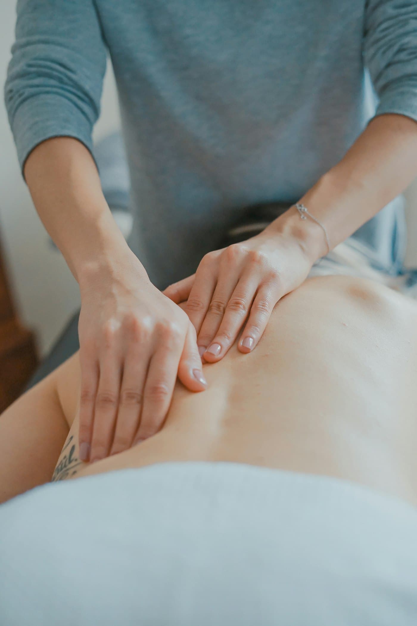 Manos de fisioterapeuta aplicando terapia manual sobre la espalda de una persona en camilla. Imagen de muestra.