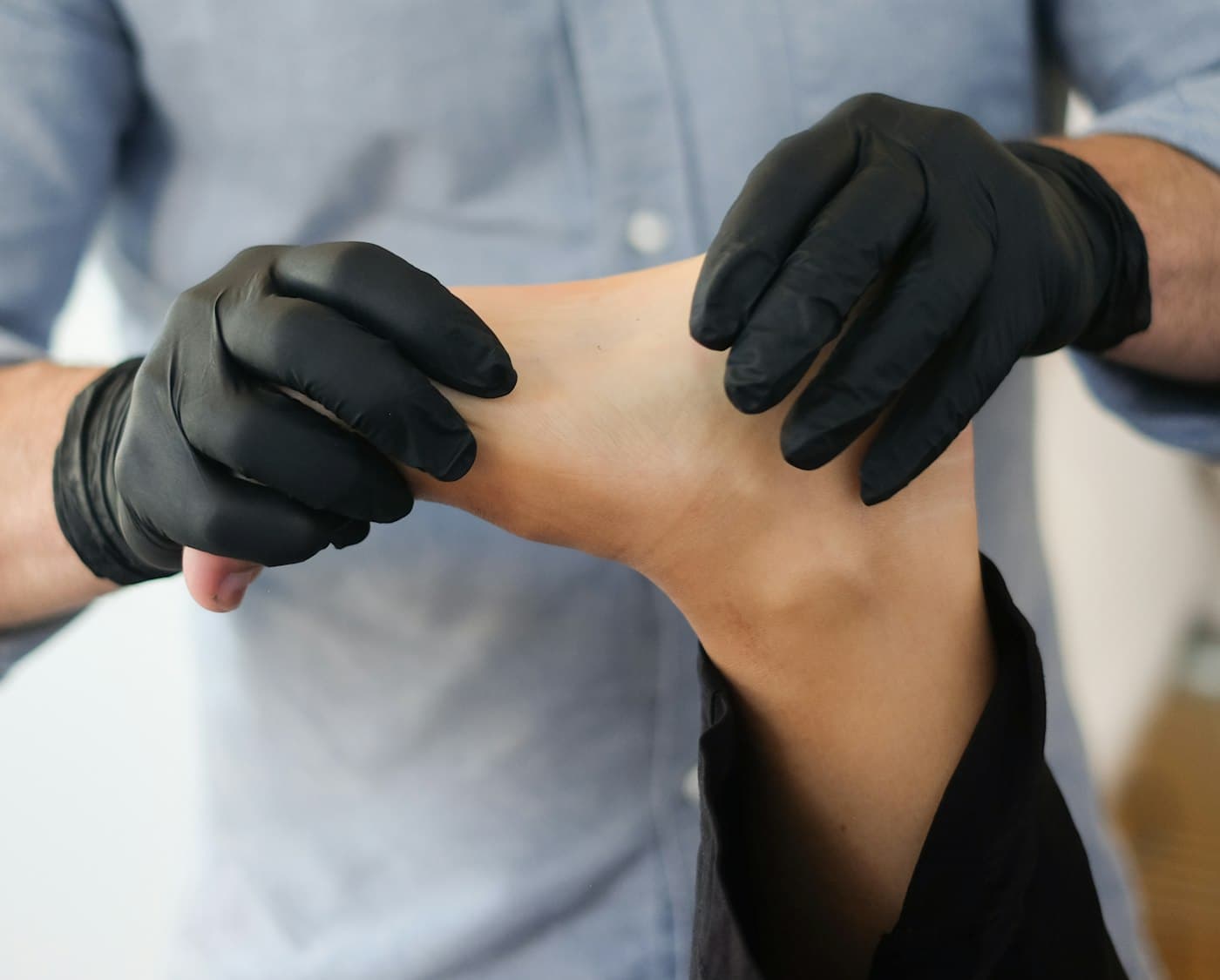 Fisioterapeuta con guantes valora con las manos el tobillo y el pie de un paciente. Imagen de muestra.